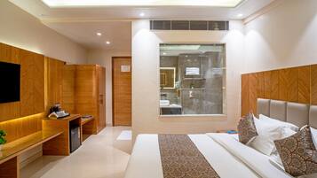 Habitación de hotel moderna con una cama grande, un escritorio, un armario y un baño visible a través de una puerta de cristal.