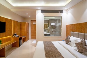 Habitación de hotel moderna con una cama grande, un escritorio, un armario y un baño visible a través de una puerta de cristal.