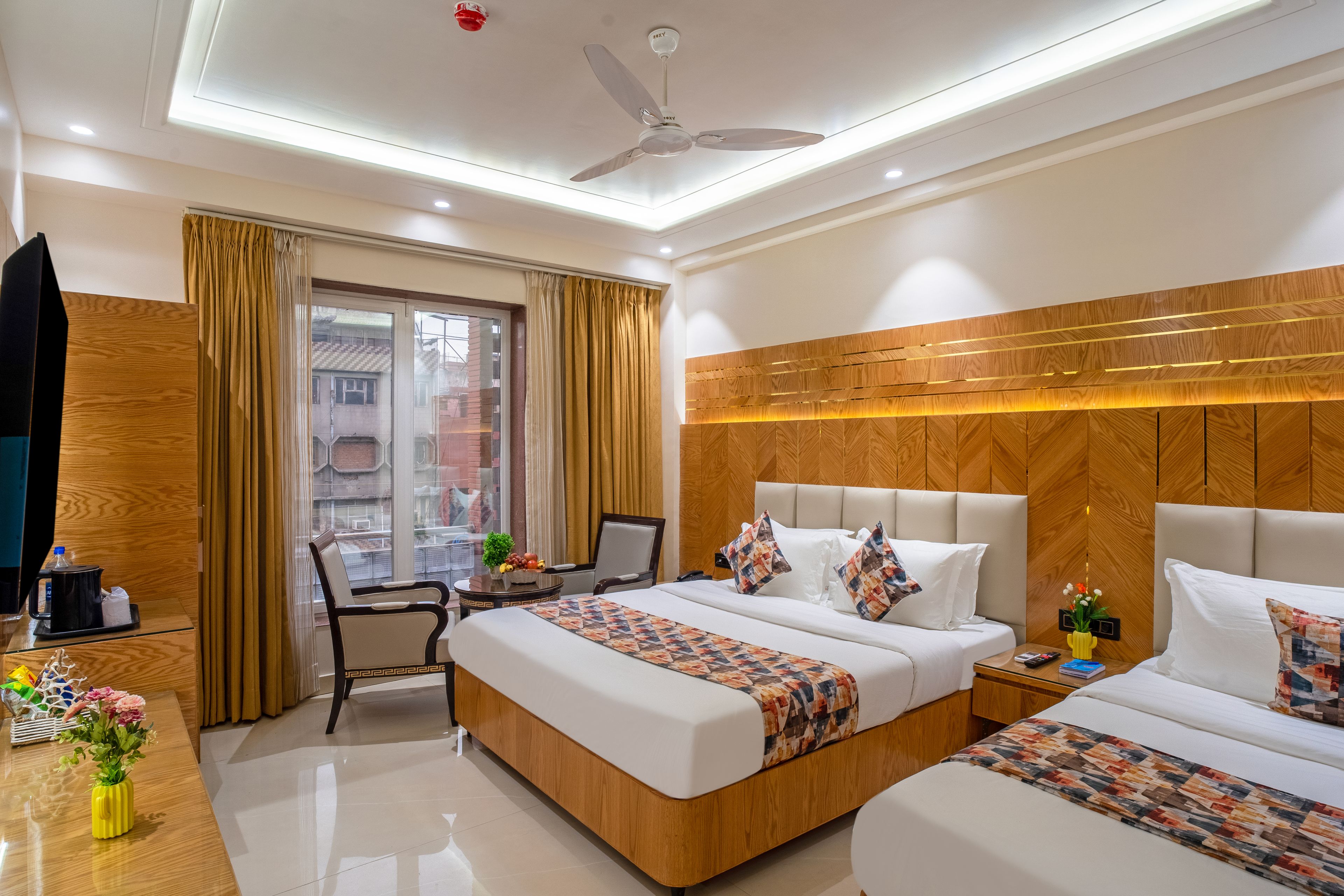 A hotel room with a bed, bedside tables, a desk, a chair, a ceiling fan, and a window with curtains.