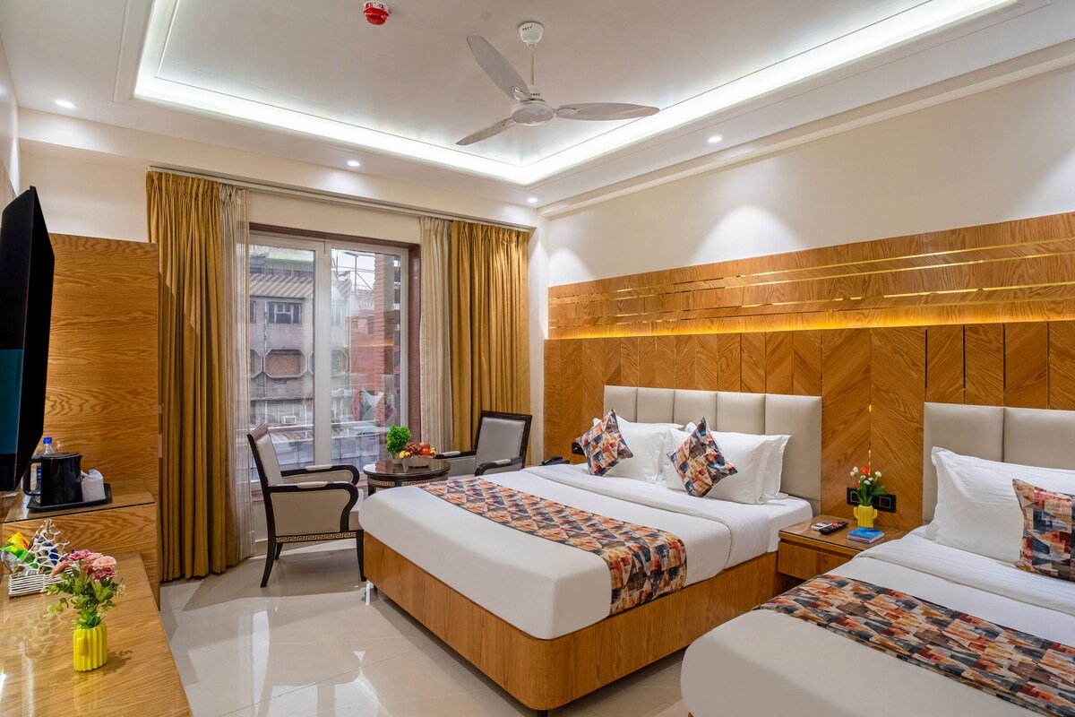 Una habitación de hotel con cama, mesitas de noche, escritorio, silla, ventilador de techo y ventana con cortinas.