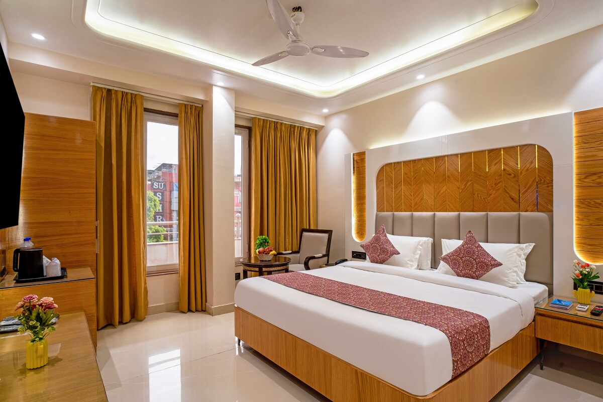Una habitación de hotel con una cama grande, un escritorio, una silla, un ventilador de techo y una ventana con cortinas.