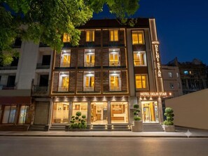 Un hotel de varios pisos con fachada moderna, ventanas iluminadas y un cartel que indica que es el 'Hotel Delhi Star'.