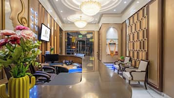 A hotel reception area with a curved reception desk, a computer, and a television screen displaying the hotel name.