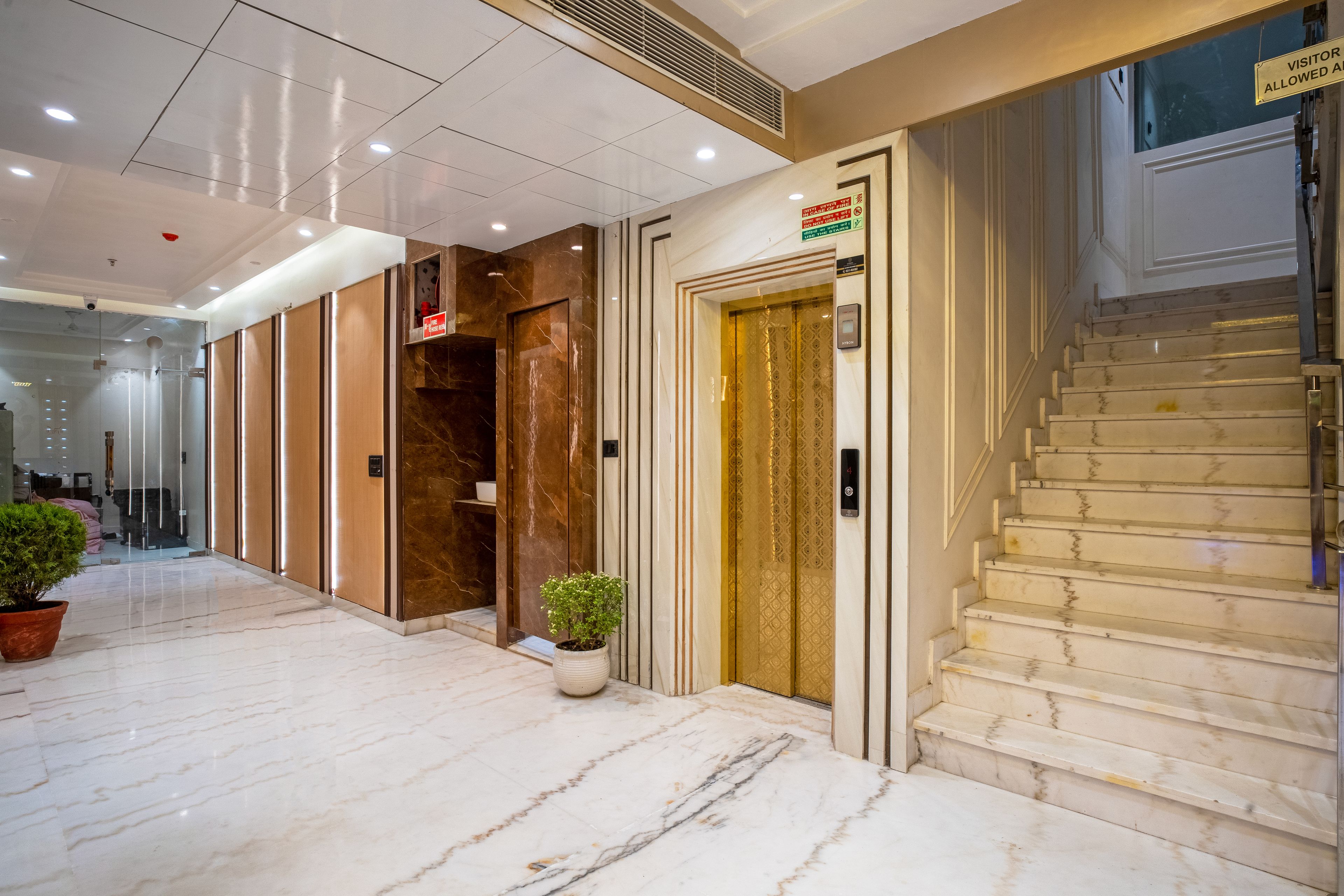 Un vestíbulo de hotel con piso de mármol, un mostrador de recepción, una escalera y una planta en maceta.