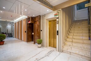 Un vestíbulo de hotel con piso de mármol, un mostrador de recepción, una escalera y una planta en maceta.