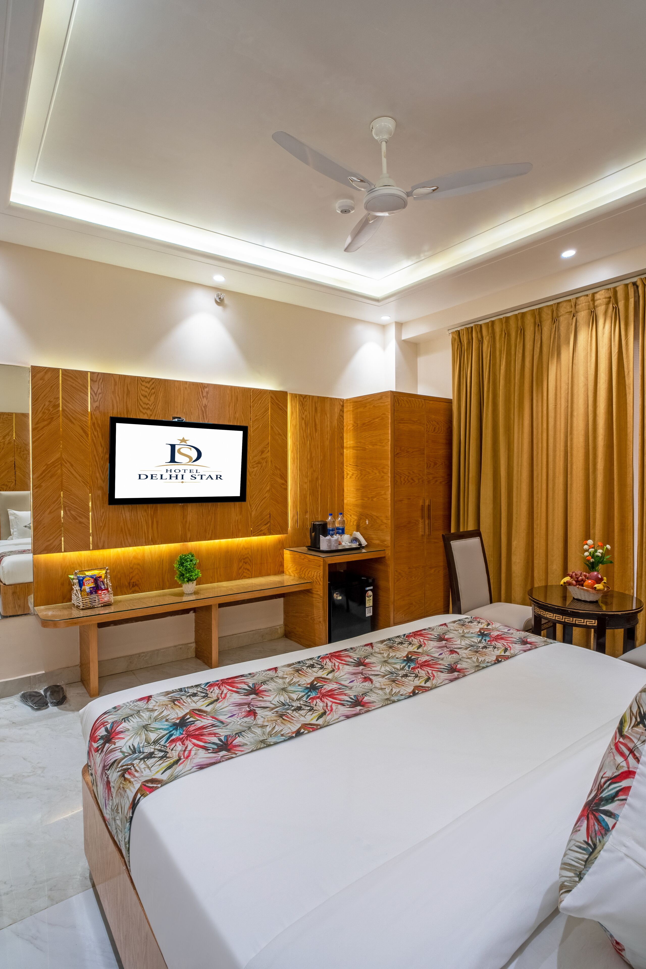 Una camera d'albergo con un letto, una scrivania, una televisione e una ventola a soffitto.