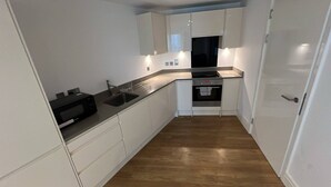 A compact kitchen with white cabinets, a black countertop, a sink, and an oven. - Abbey Nest - 1 Bedroom (London)