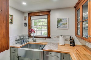 A kitchen with a built-in dishwasher, a window with a view, and a wooden cabinet. - Serene Coastal Getaway: 2 Mi to Newport & Beaches (Middletown)