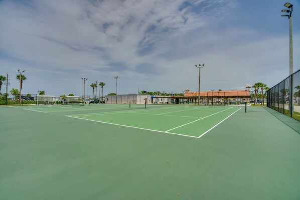 Ein Tennisplatz mit grüner Belag, umzäunt und unter blauem Himmel.