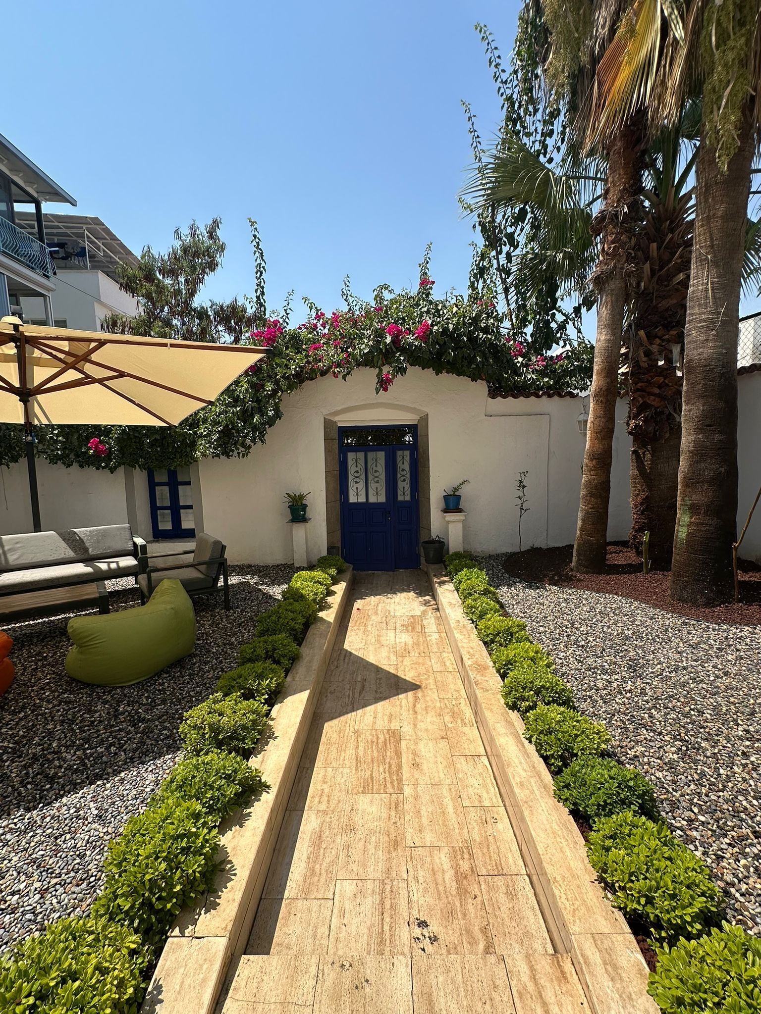 A pathway leading to a blue door, surrounded by greenery and palm trees.