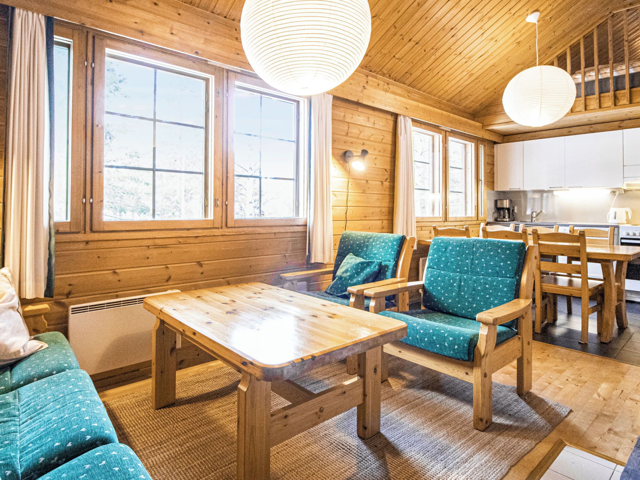 A cozy cabin interior with wooden walls, large windows, a dining area, and a kitchen.