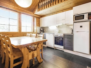 Una mesa de madera con sillas, una cocina con armarios blancos, un microondas y un refrigerador.