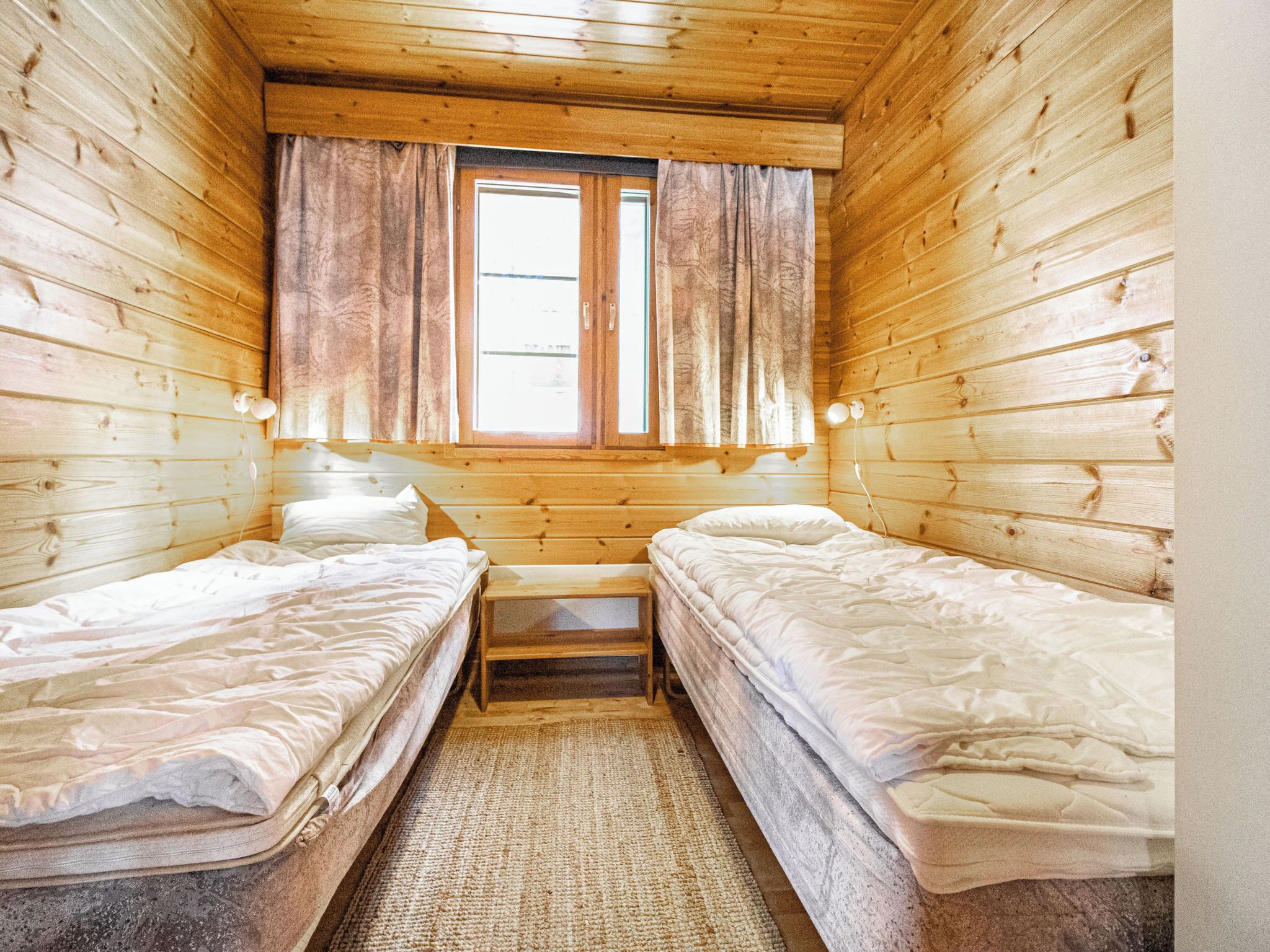 A small, cozy room with two single beds, a bench, and a window with curtains.