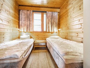 Una habitación pequeña y acogedora con dos camas individuales, un banco y una ventana con cortinas.