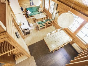 L’intérieur d’un chalet en bois comprend un canapé, une table à manger et des chaises, une cheminée et de grandes fenêtres.