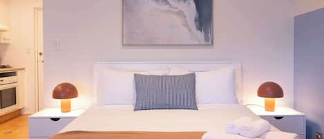 A hotel room with a bed, two bedside lamps, a painting, and a neatly made bed with towels.