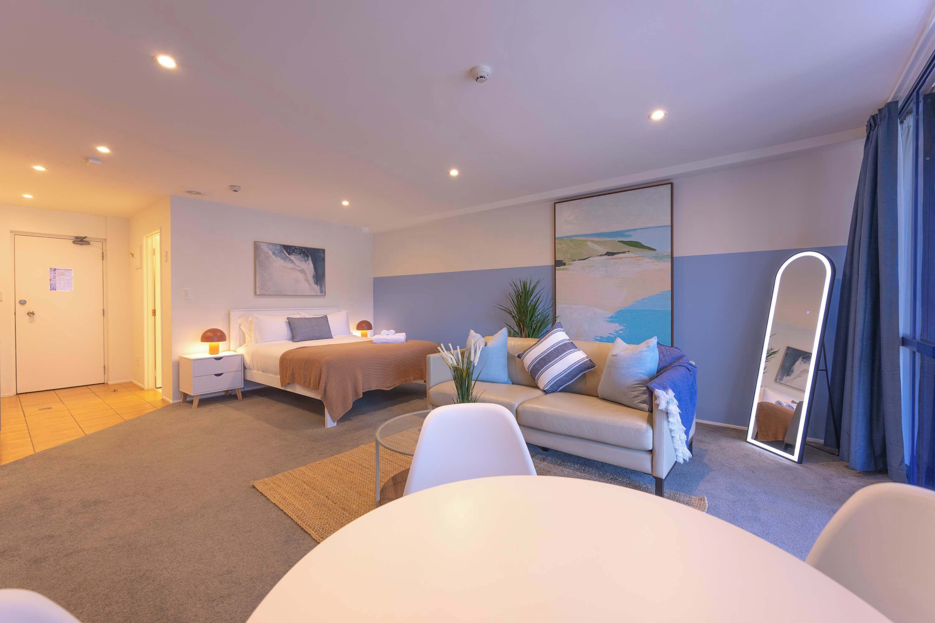 Ein Hotelzimmer mit Bett, Sofa, Esstisch, Spiegel und einem Bild an der Wand.