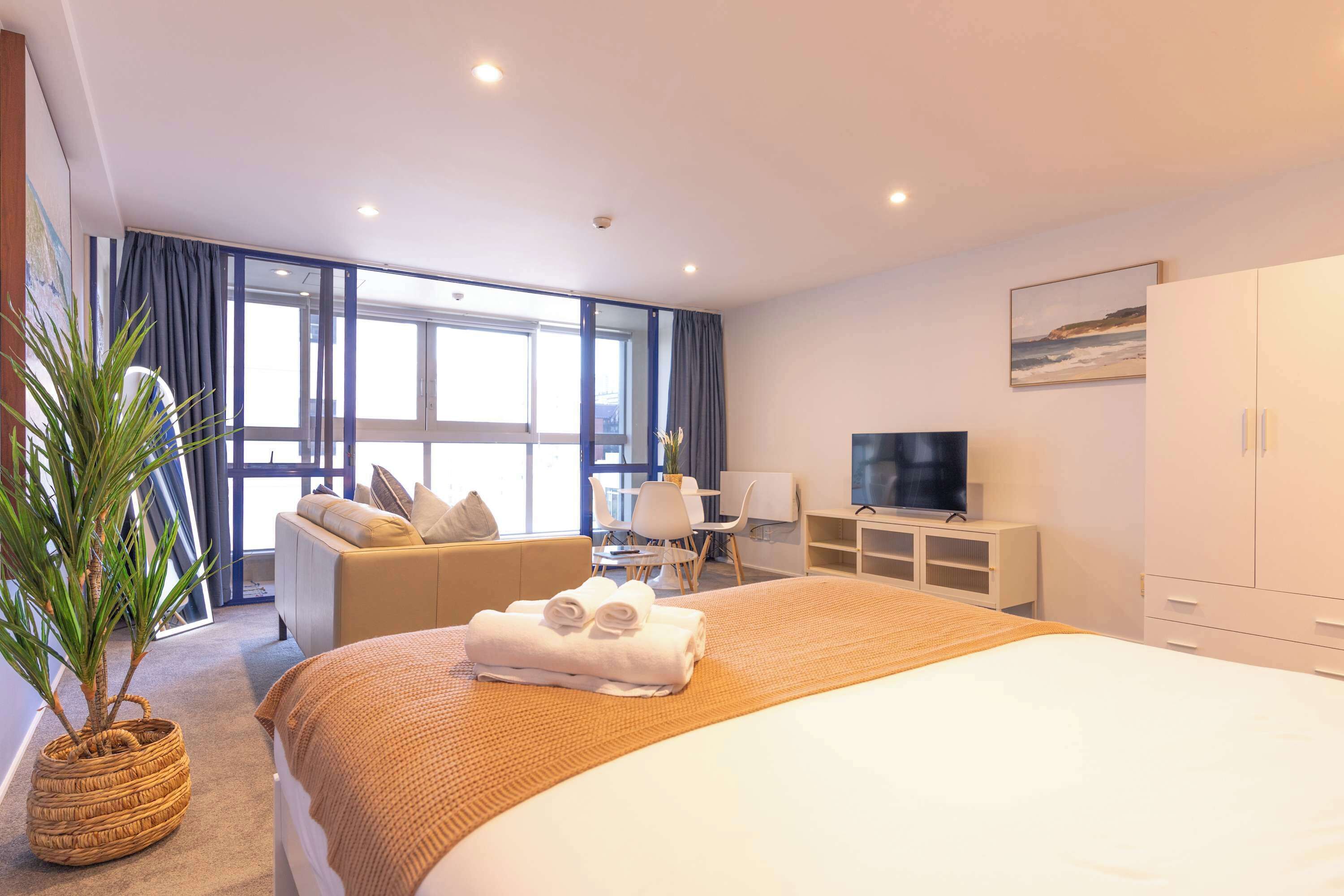 Hotelkamer met een groot bed, een bank, een bureau, een televisie en een potplant.