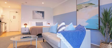 A modern hotel room with a bed, a sofa, a coffee table, and a painting on the wall.