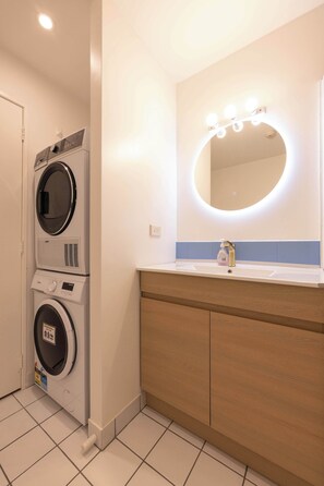 Ein modernes Badezimmer mit integrierter Waschmaschine, einem Waschtisch mit Spiegel und einem Waschbecken.