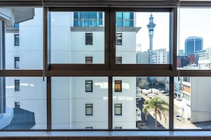 Blick durch ein Fenster auf ein mehrstöckiges Gebäude mit einem markanten Turm und einem Parkplatz mit Palmen.