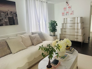Un salon avec un canapé, une table basse sur laquelle sont posés des livres et une plante, un meuble blanc et, au mur, un tableau représentant un paysage urbain.