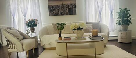 A living room with a sofa, armchair, coffee table, and a potted plant.