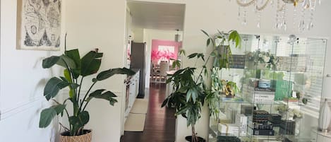 A hallway with a chandelier, potted plants, and a glass display case with books.