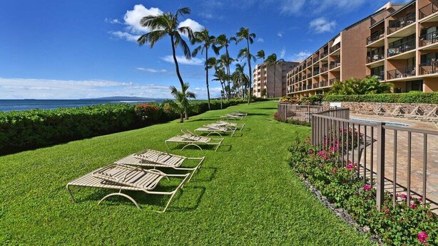 A hotel with a poolside area, lounge chairs, palm trees, and a view of the ocean. - Ocean-view 1BR condo with pool, AC and beach access-Maalaea Banyans 112 (Wailuku)