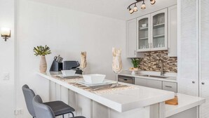 A modern kitchen with a central island, white cabinetry, and a backsplash. - Ocean-view 1BR condo with pool, AC and beach access-Maalaea Banyans 112 (Wailuku)