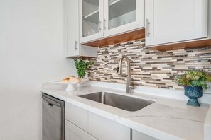 A kitchen with a modern design, featuring a stainless steel sink, white cabinets, and a mosaic tile backsplash. - Ocean-view 1BR condo with pool, AC and beach access-Maalaea Banyans 112 (Wailuku)