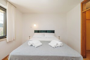 Un lit bien fait, avec deux serviettes enroulées, une tête de lit et une lampe de chevet.