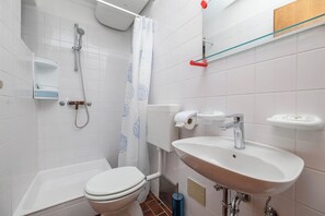 Un bagno con il water, doccia, lavandino e uno scaffale in vetro.