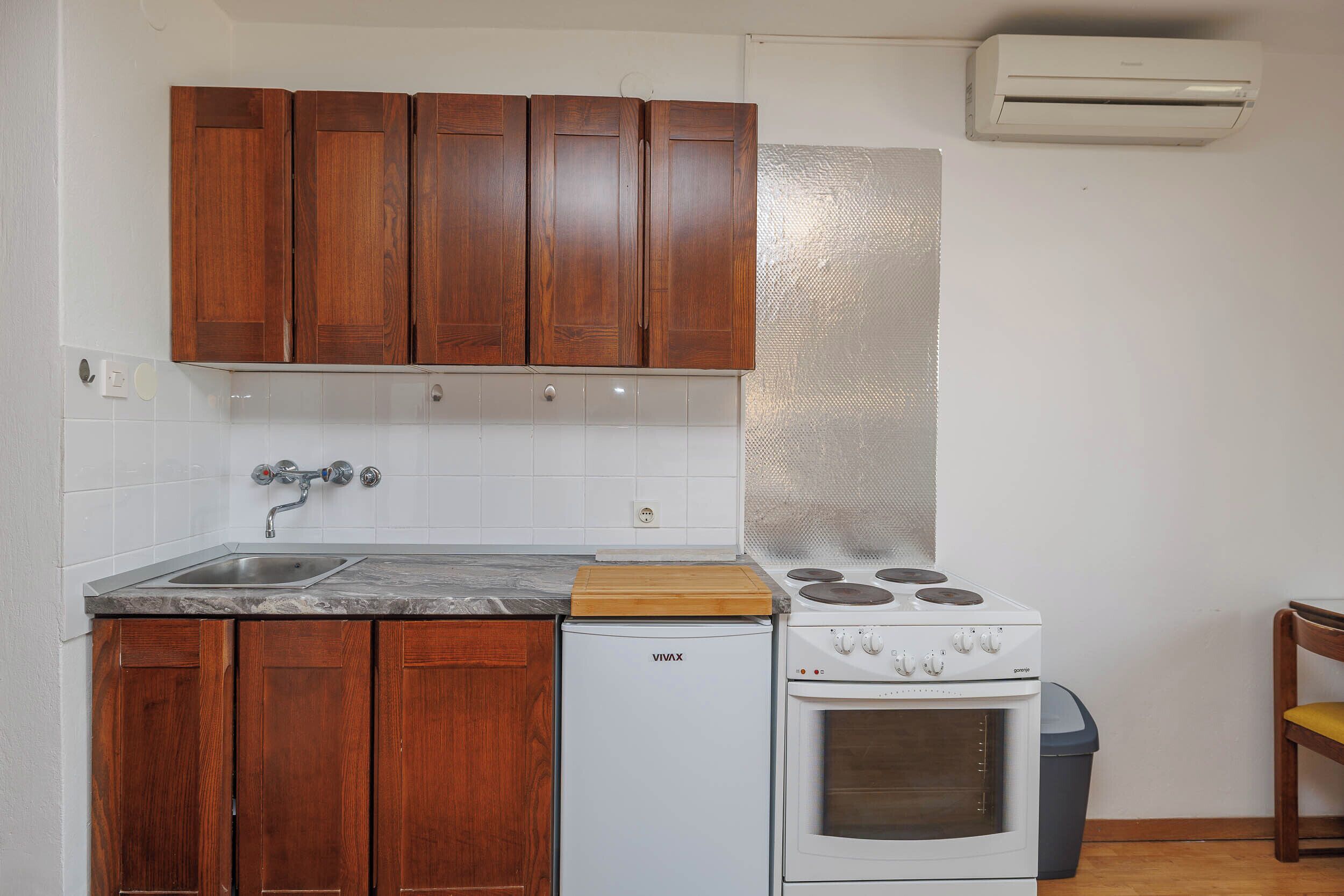 A kitchen with wooden cabinets, a white refrigerator, a stove, and an air conditioner.