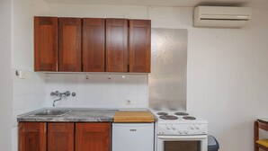 A kitchen with wooden cabinets, a white refrigerator, a stove, and an air conditioner. - Charming Studio in Malinska (Malinska-Dubašnica)