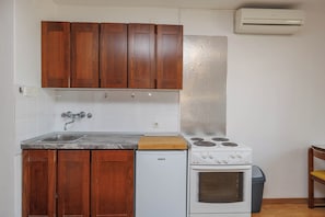Eine Küche mit Holzschränken, einem weißen Kühlschrank, einem Herd und einer Klimaanlage.