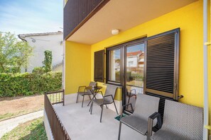 Ein Balkon mit Tisch und Stühlen, eine gelbe Wand und ein Fenster mit Rollläden.