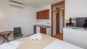 Hotellihuone, jossa on sänky, pieni keittonurkkaus, tuoli ja televisio.
