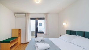 Habitació d'hotel amb llit, una banca de fusta, una finestra amb cortines i vista al balcó.