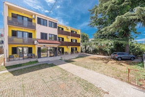 A multi-story building with balconies, a paved driveway, and a parked car. - Cozy Studio Retreat in Malinska-Dubašnica with Garden View (Malinska-Dubašnica)