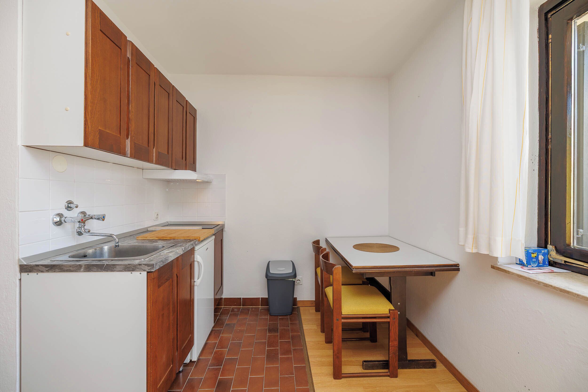 Una cucina compatta con lavello, mobili in legno, un tavolino e una finestra con tende.
