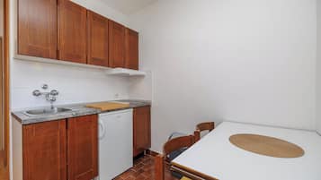 Cocina compacta con armarios de madera, encimera blanca, un lavamanos y una pequeña mesa con un mantel tejido.