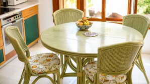 A round dining table with chairs, a bowl of fruit, and a kitchen area with a microwave and cabinets. - Villa Günbatımı (Kaş)