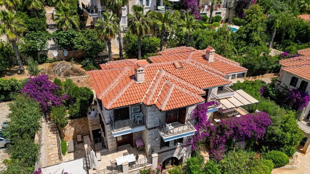 A multi-story house with a red-tiled roof, surrounded by lush greenery and purple bougainvillea. - Villa Günbatımı (Kaş)
