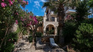 A stone pathway leading to a building with a stone facade, two lounge chairs, and lush greenery. - Villa Günbatımı (Kaş)