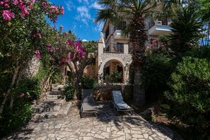 A stone pathway leading to a building with a stone facade, two lounge chairs, and lush greenery. - Villa Günbatımı (Kaş)