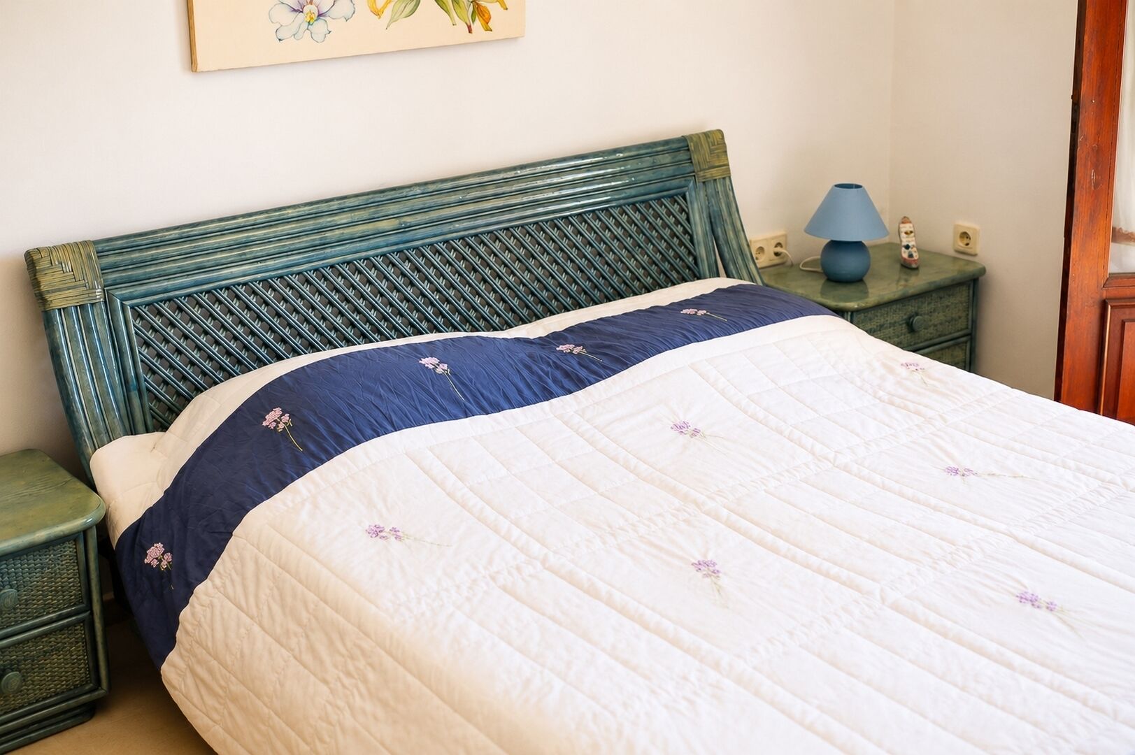Una cama con cabecera acolchada, una mesita de noche, una lámpara y un cuadro colgado en la pared.