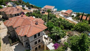 A coastal residential area with terracotta-roofed buildings, a clear view of the sea, and lush greenery. - Villa Günbatımı (Kaş)