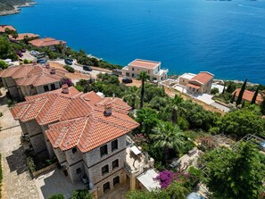 A coastal residential area with terracotta-roofed buildings, a clear view of the sea, and lush greenery. - Villa Günbatımı (Kaş)