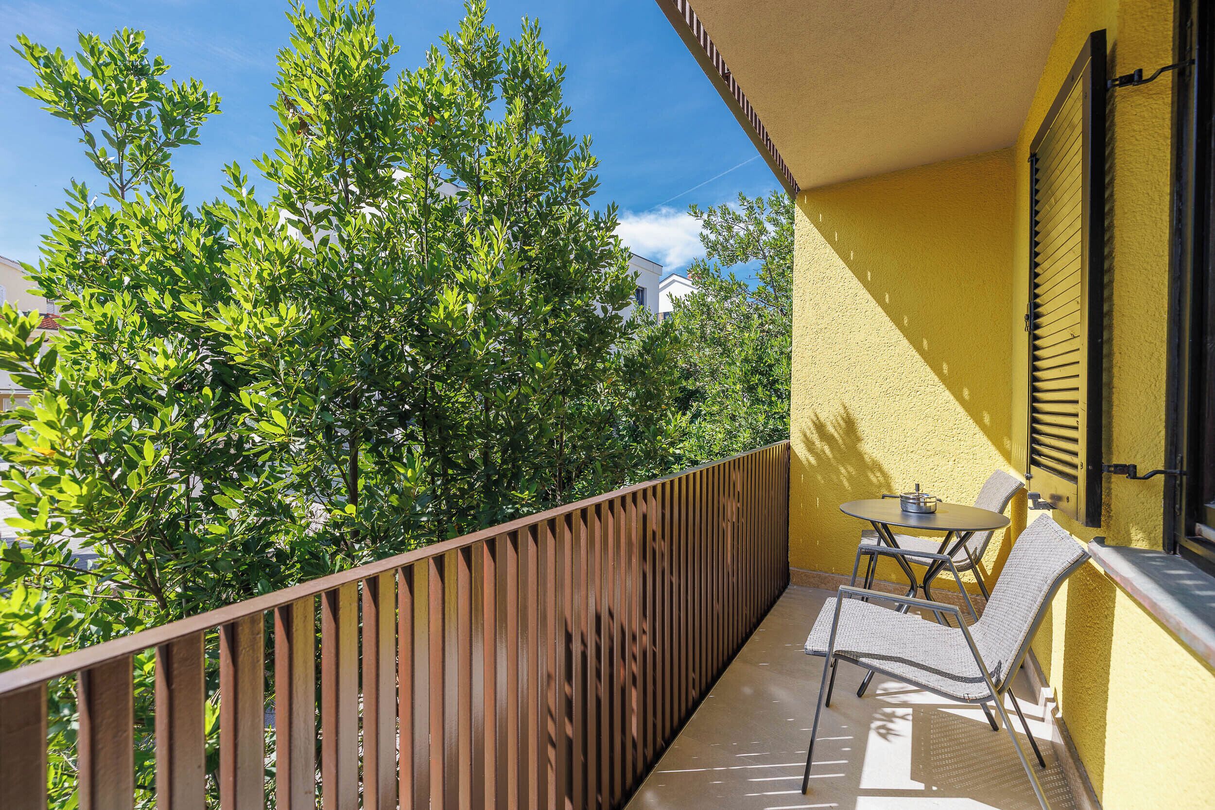 A balcony with a table and chairs, a wooden railing, and a yellow wall.